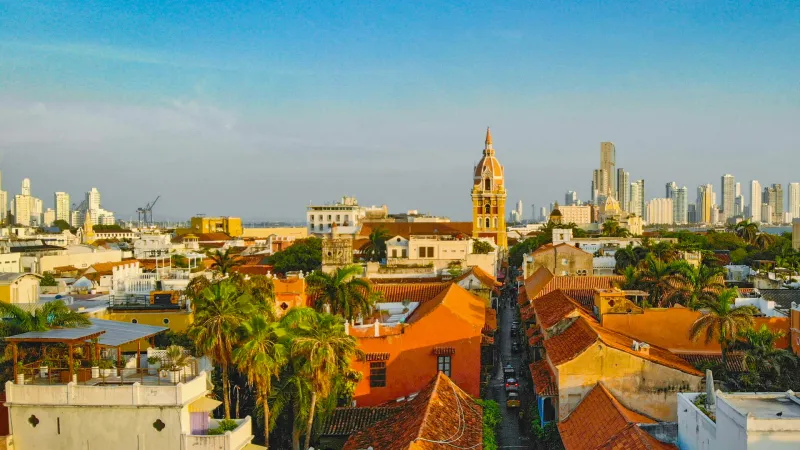 Terracotta rooftops and palms of Cartagena's walled old town in late afternoon light, with the cathedral bell tower and the Bocagrande high-rises beyond
