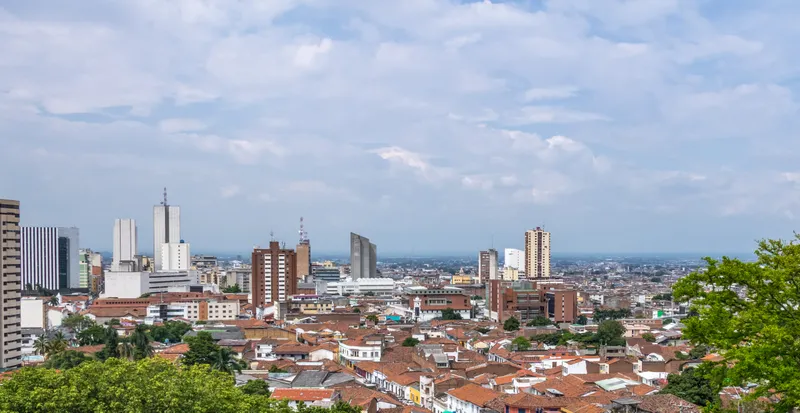 Cali's downtown rooftops and mid-rise towers seen from a hillside, with the Cauca valley flattening out to the horizon