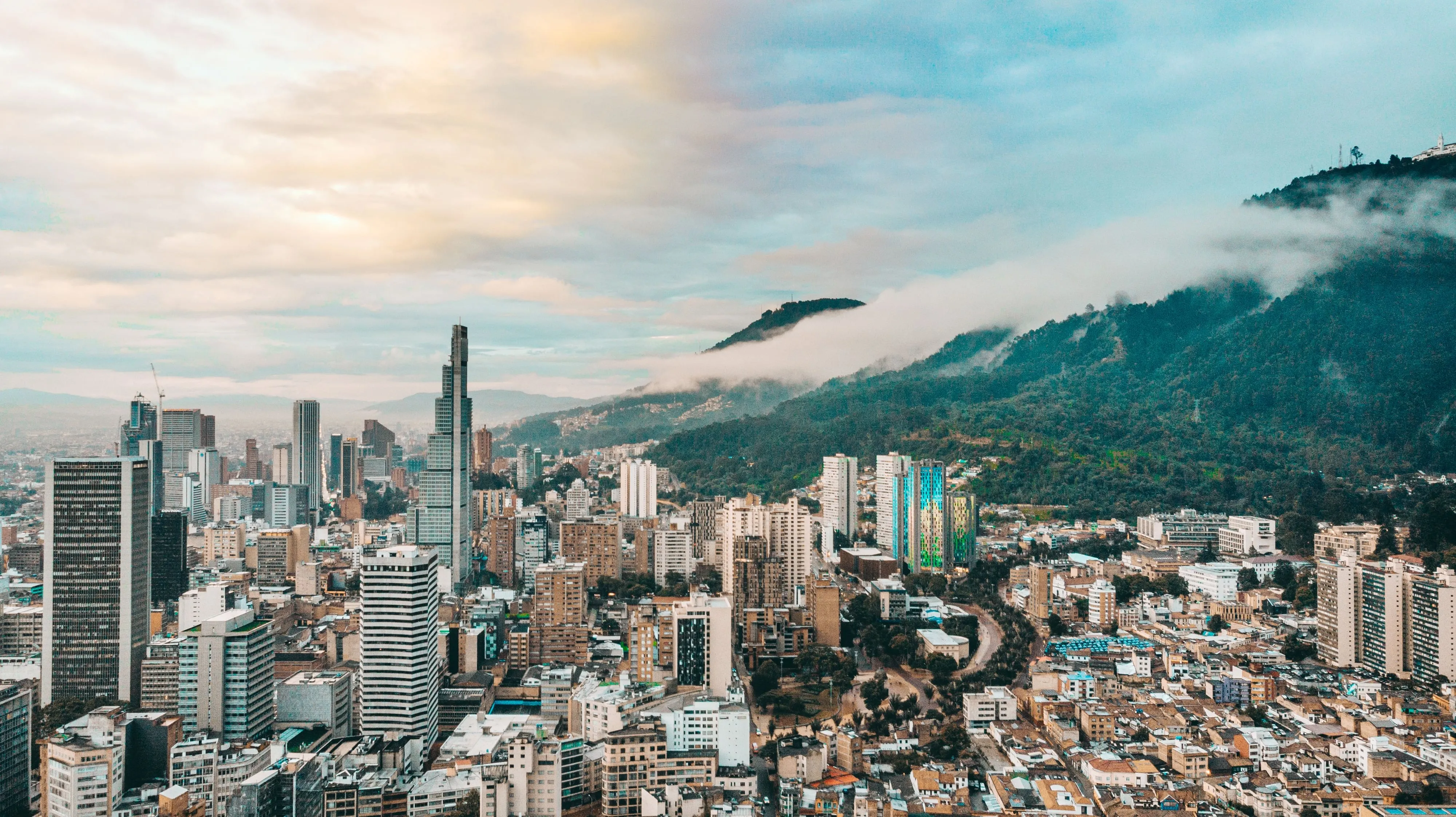 Bogotá's high-rise skyline with cloud spilling over the forested eastern hills behind it