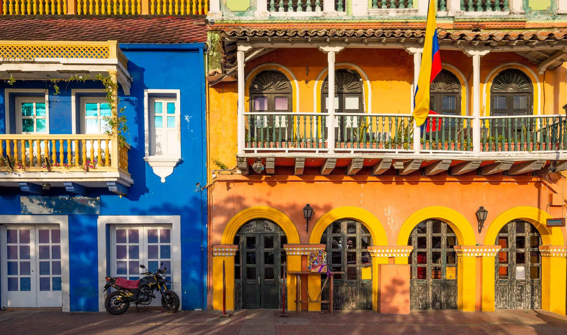 A narrow colonial street in Cartagena lined with brightly painted balconied houses and hanging flowers