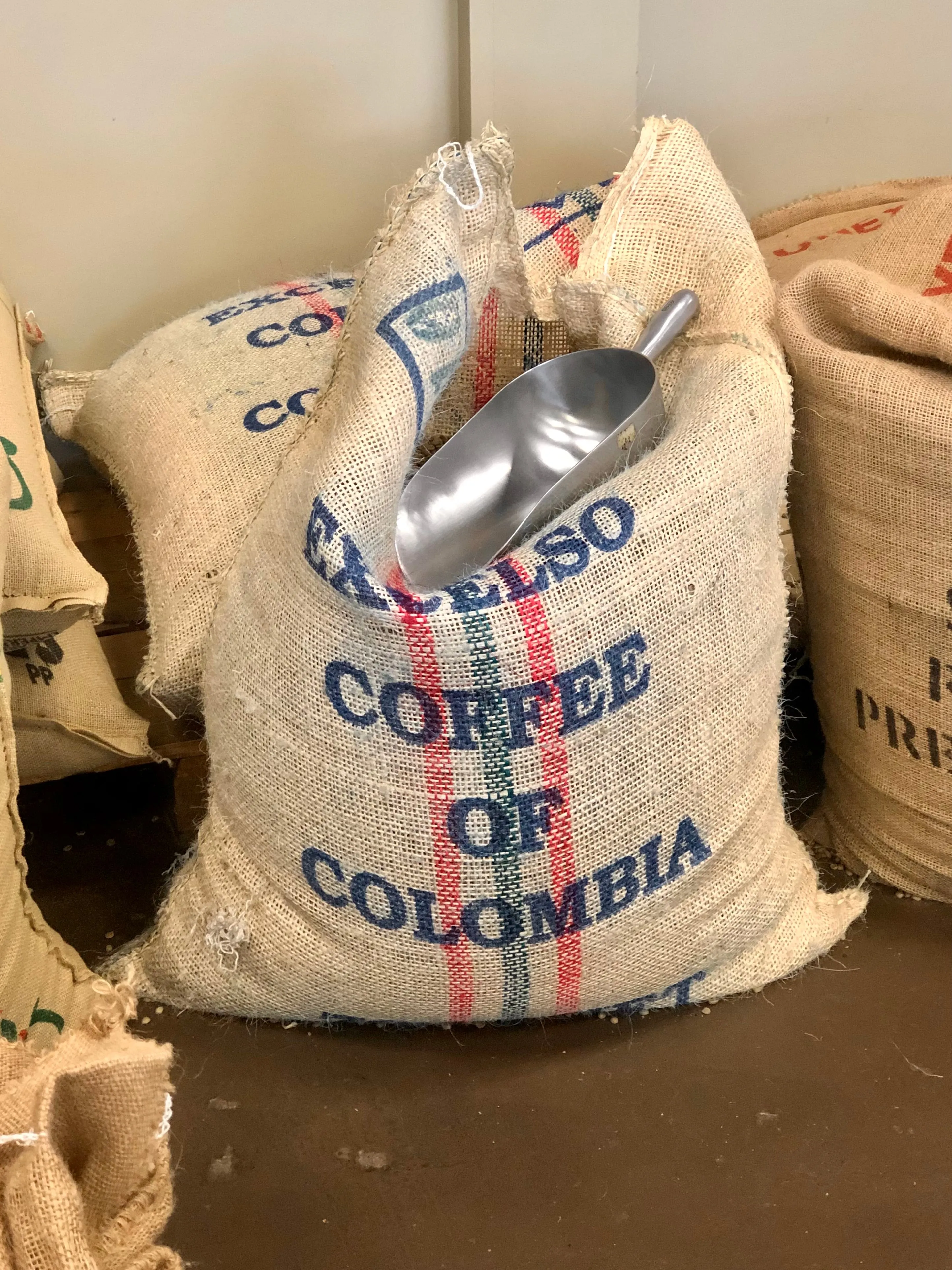 Burlap sacks of Colombian Excelso coffee beans with a metal scoop resting on top