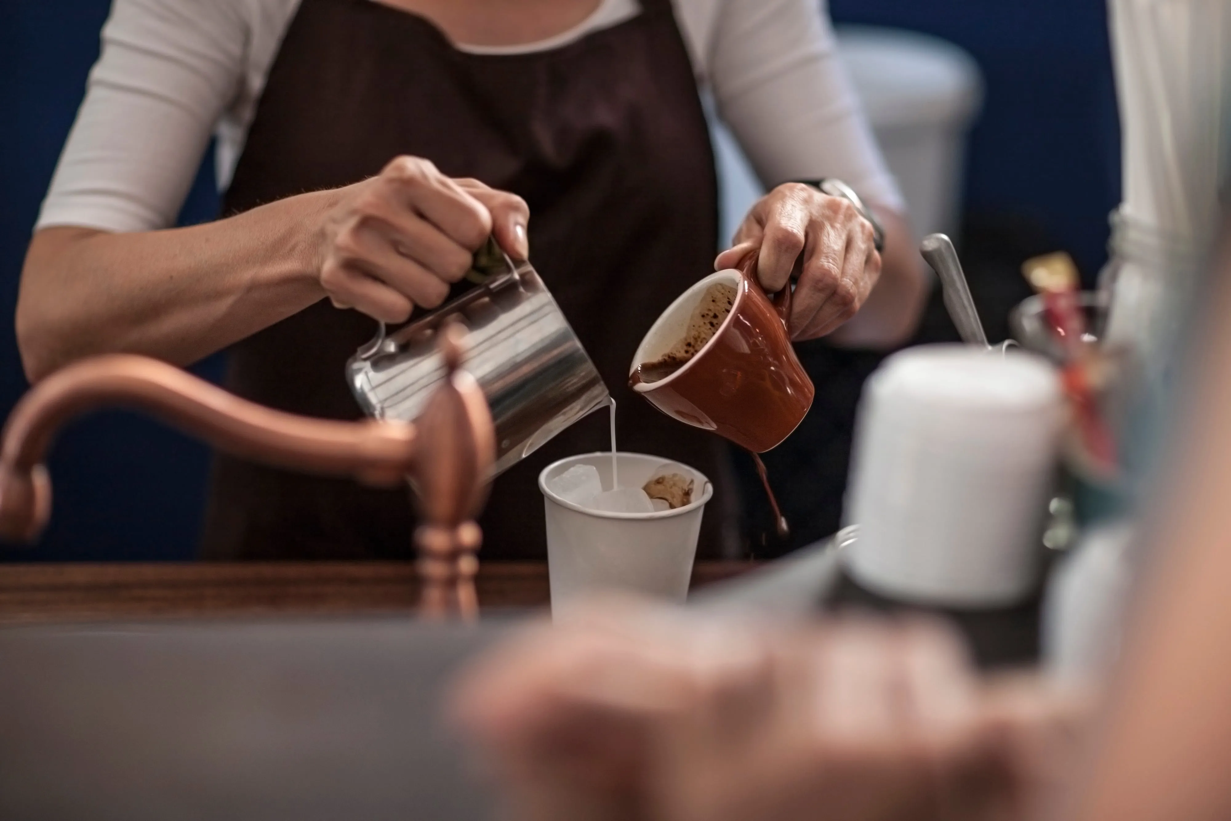 A barista pouring steamed milk and freshly brewed coffee into a cup