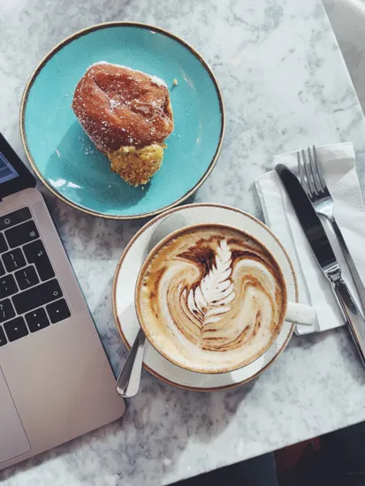 Coffee and pastry on a cafe table next to a laptop.