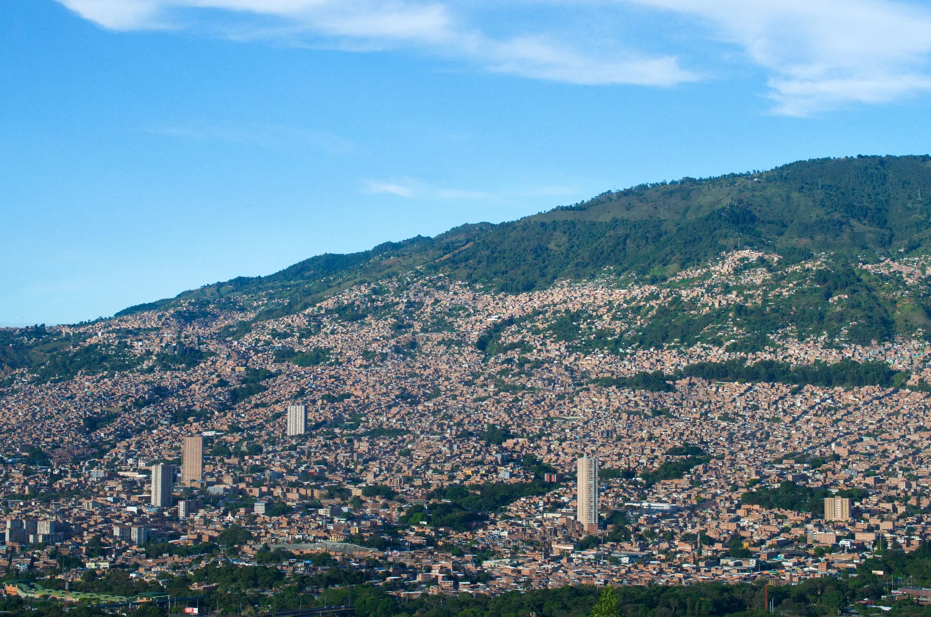 Medellin filling the Aburra valley in clear daylight, houses running up the hillsides to a green ridge